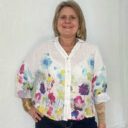 Lady showing floral detail on Italian linen top in white.